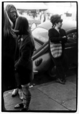 Group of young people talking on a sidewalk; to the side a woman leans against a VW Bug across from Pacific Drugs